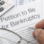 Close up of bankruptcy petition with calculator and writing hand